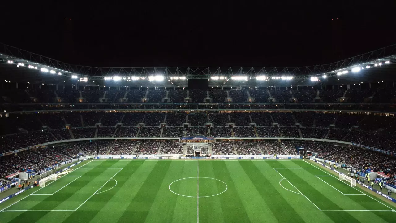 Estadio de fútbol iluminado durante un partido nocturno visto desde la grada alta