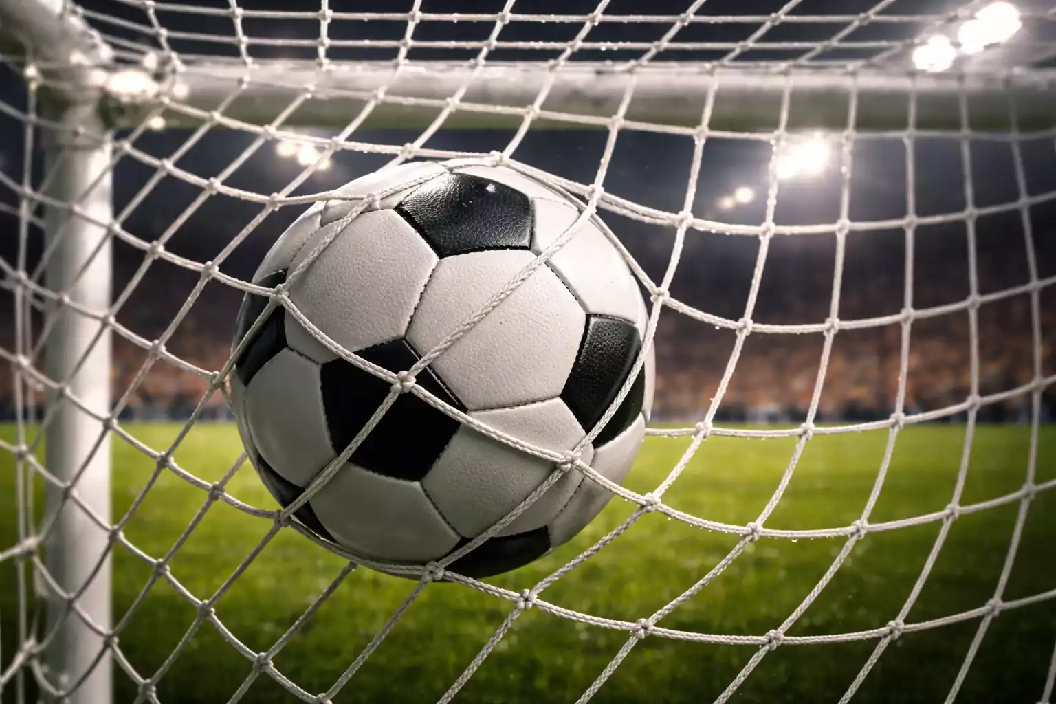 Red de una portería de fútbol agitándose tras un gol con el césped iluminado por focos